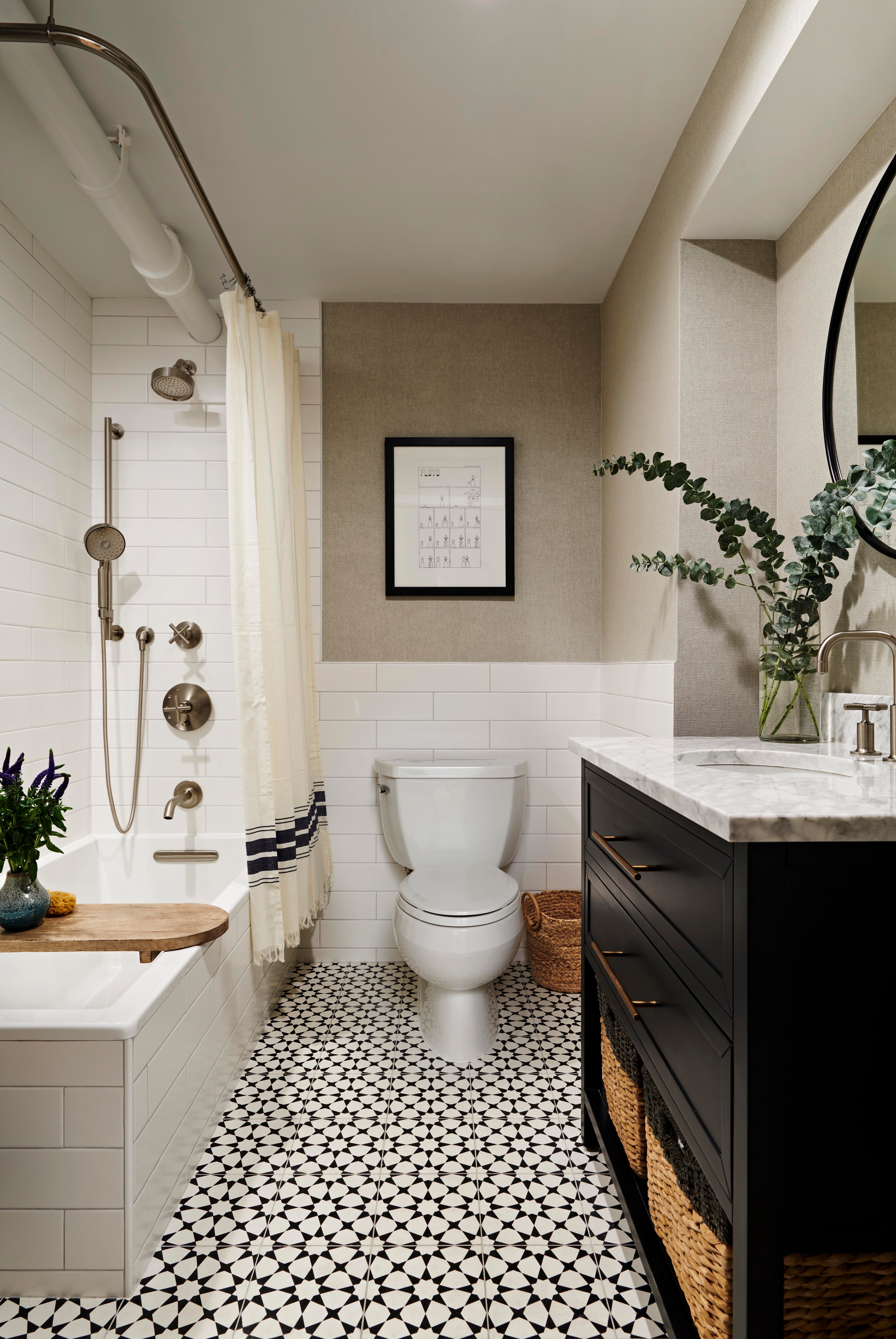 A remodeled bathroom in Tribeca New York City featuring a tub-shower combo with brushed nickel fixtures, white subway tile walls, patterned floor tile, and a large black storage vanity.