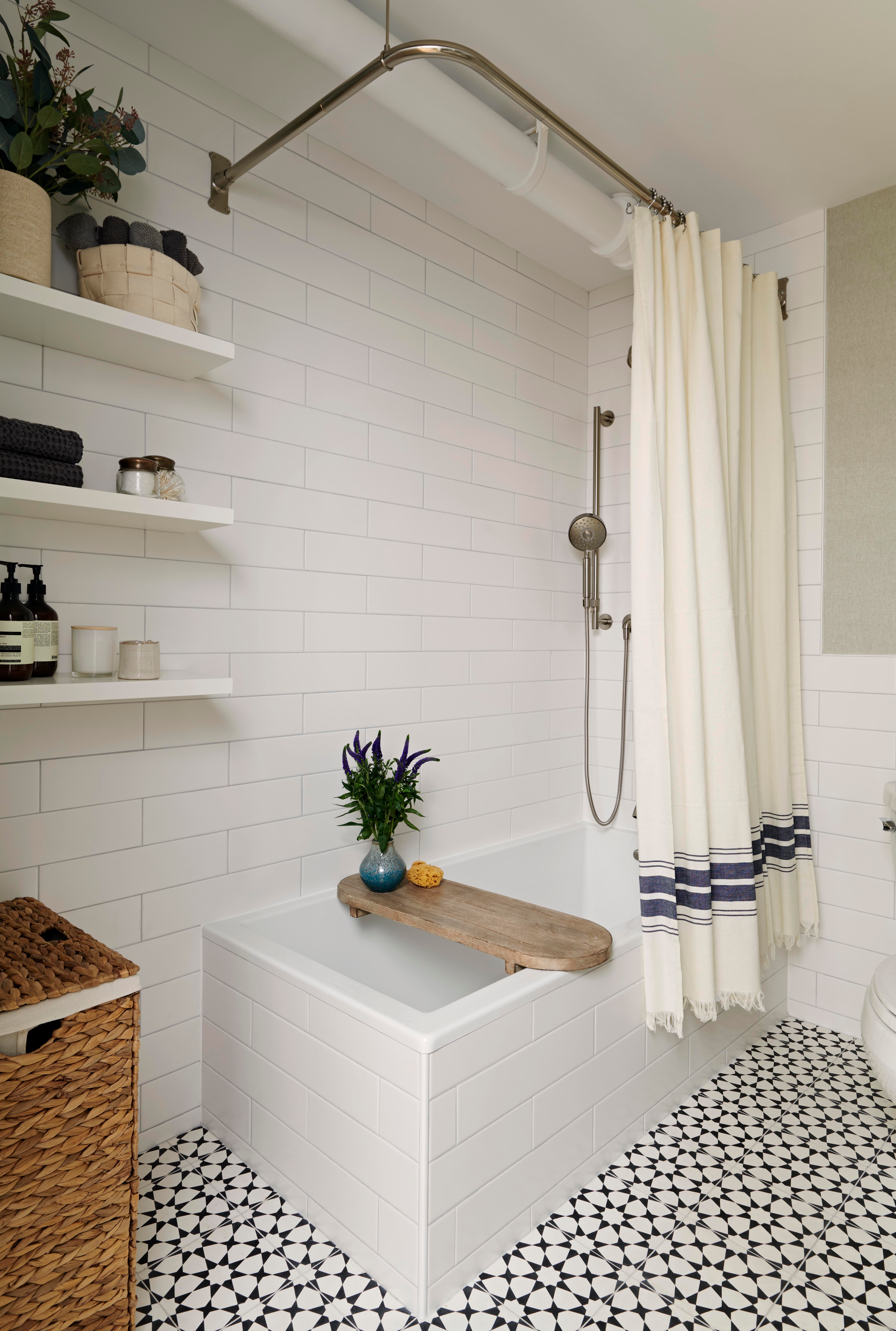 New York bathroom with a bathtub, patterned floor tile, white subway tile, floating shelves, and a hamper to store towels