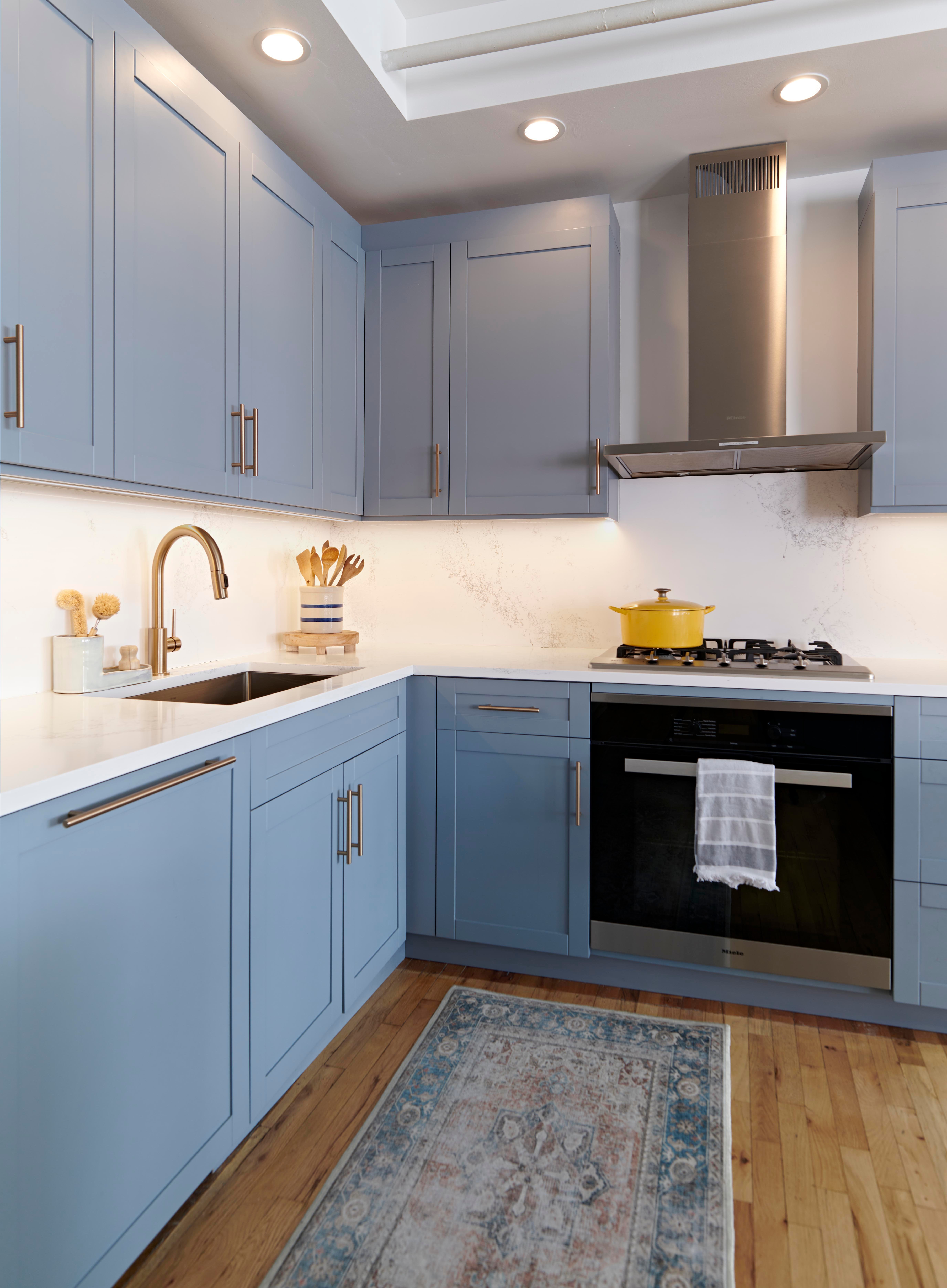 Kitchen remodel with light blue shaker cabinets, hardwood floors, white countertops, stainless steel appliances, and brushed nickel fixtures