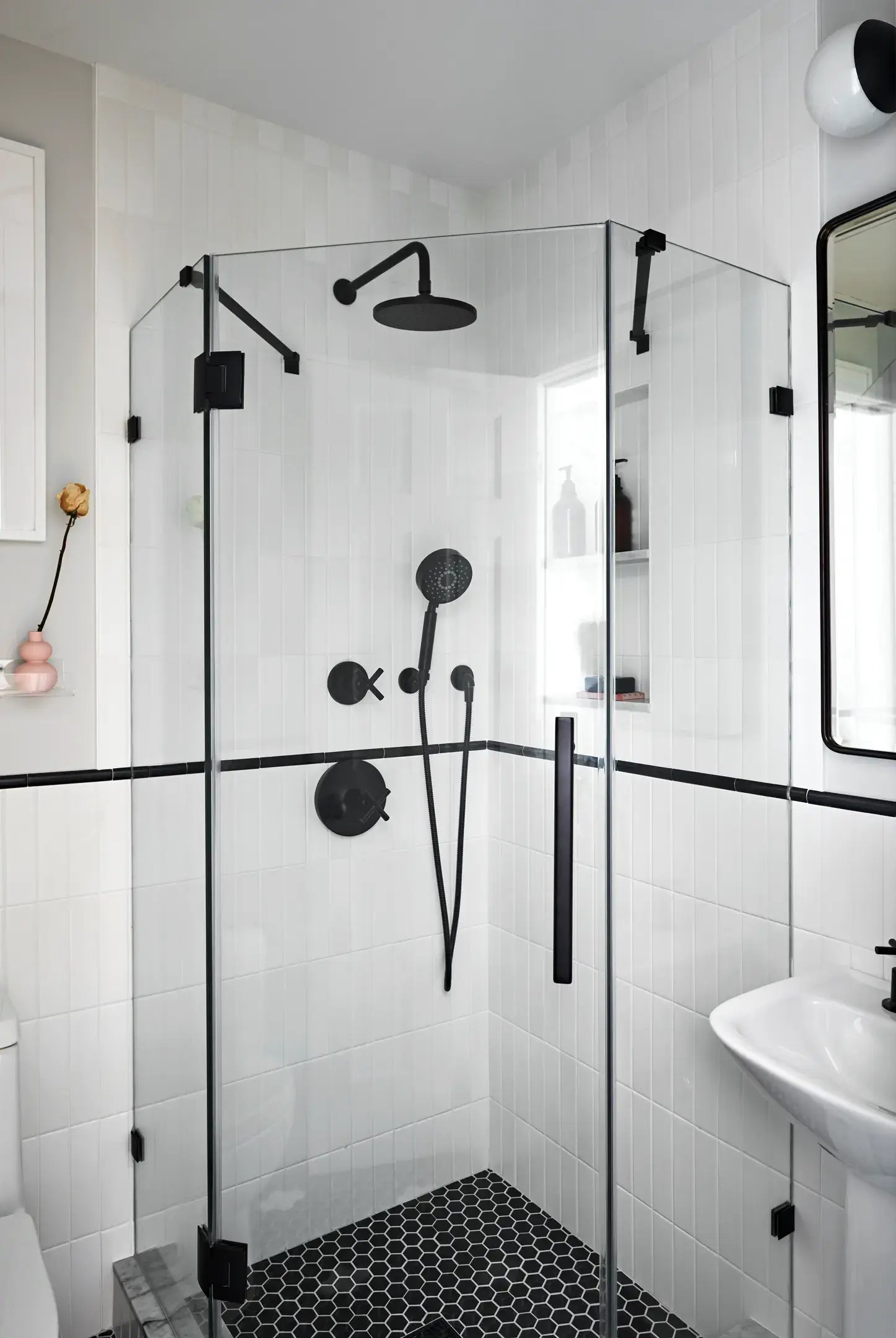 White tile corner shower with black hardware and hex floor.