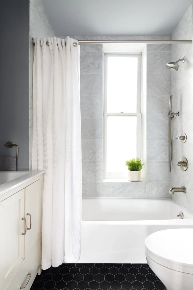 Bright bathroom with tub, shower, curtain, and window.