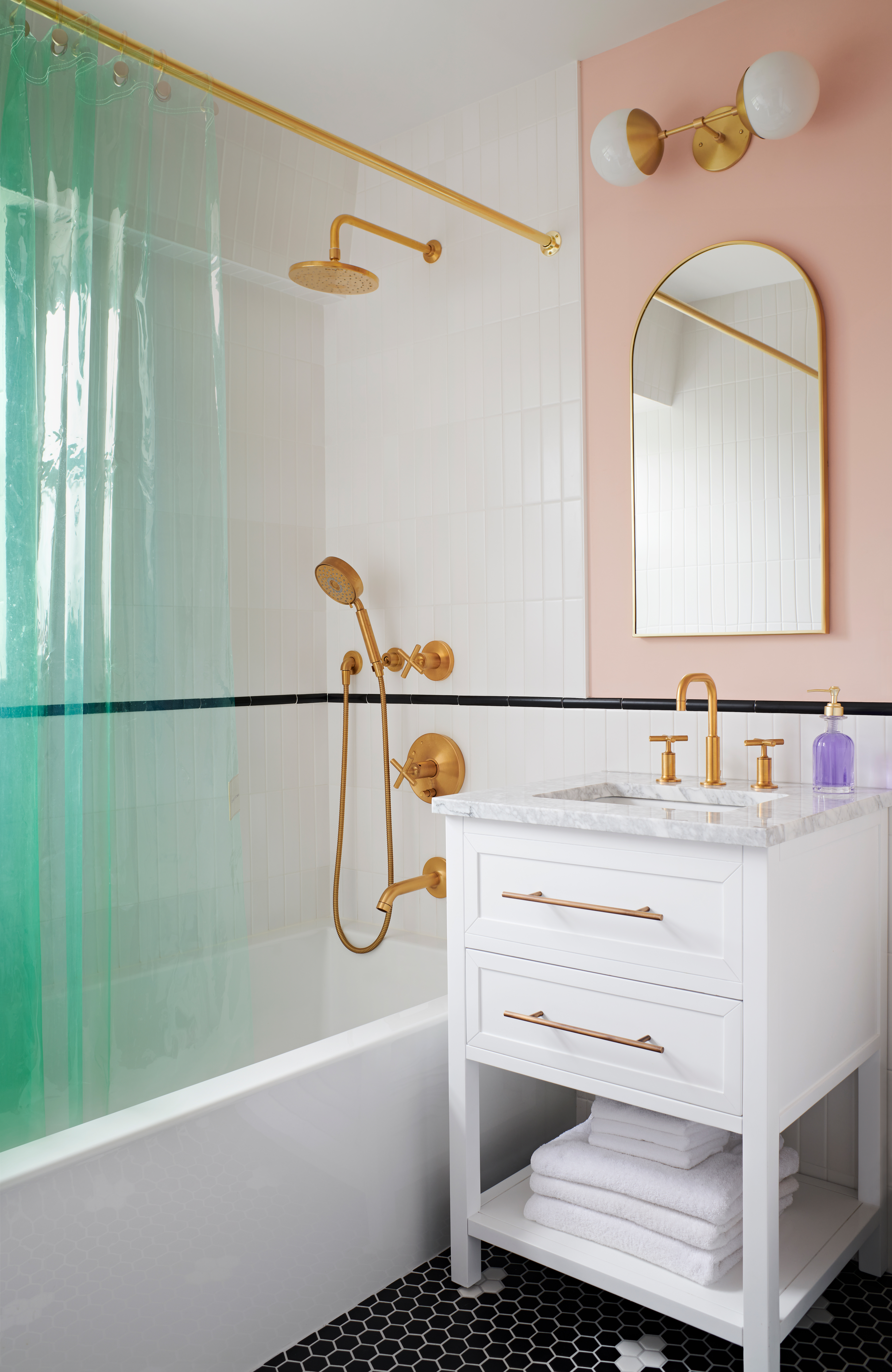 Brooklyn New York classic bathroom with black and white hexagonal flooring, white subway tiles, brass fixtures, blush pink walls, and a green shower curtain