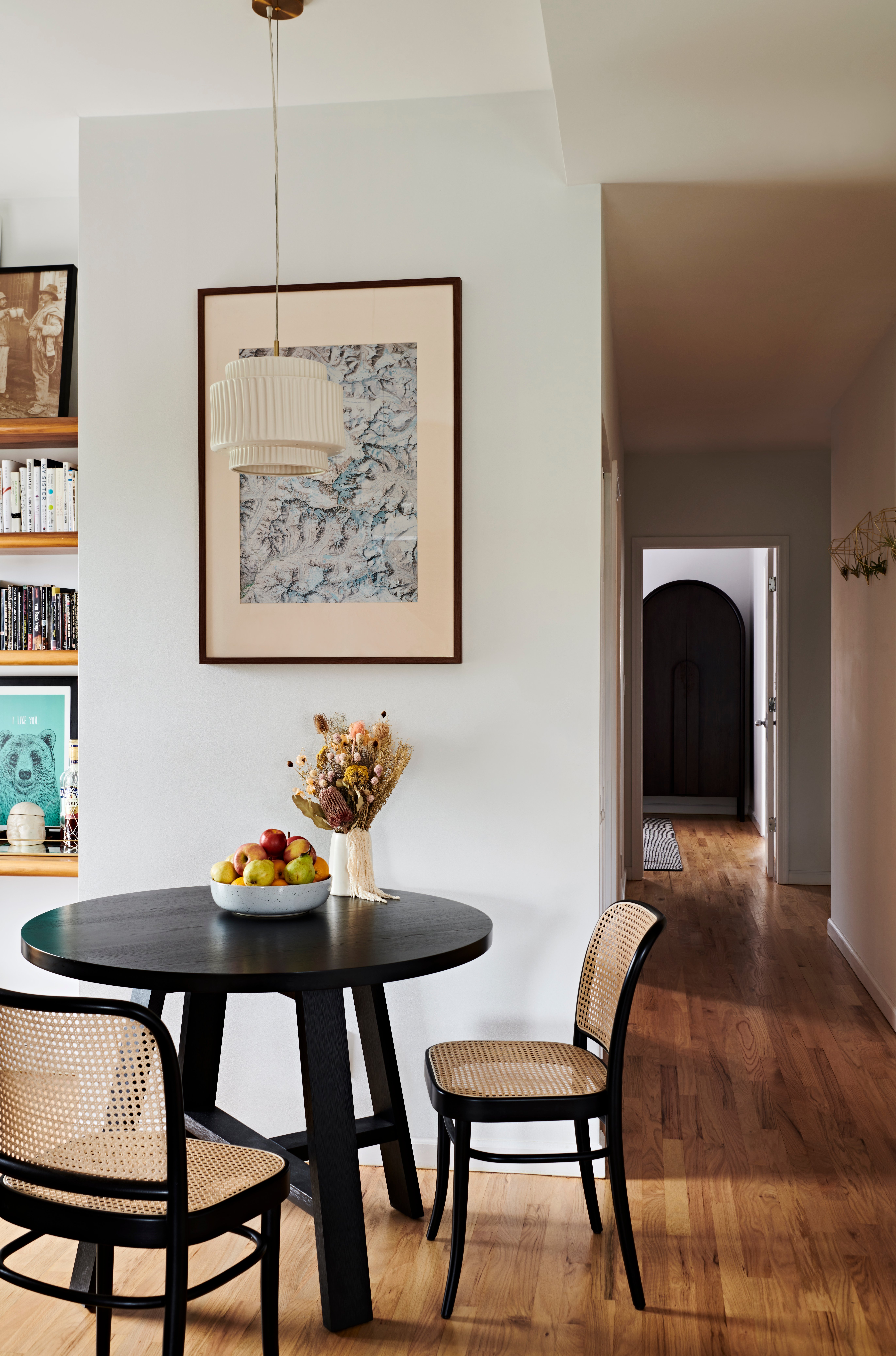 Breakfast nook with bookshelves, hardwood floor, a black wood table, and cane chairs
