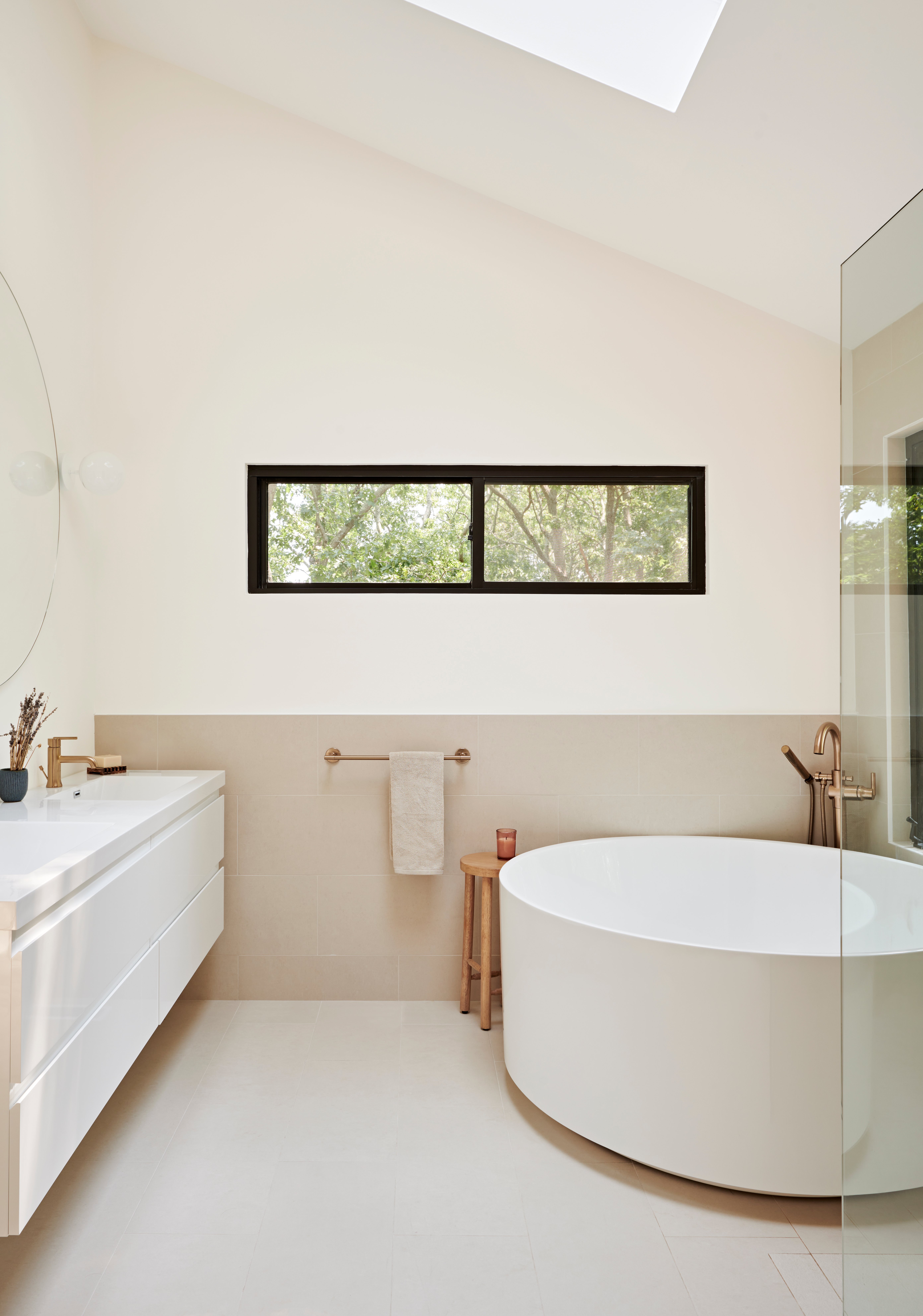 Contemporary luxury bathroom with round soaking tub, white double vanity, beige wall tiles, and a neutral palette