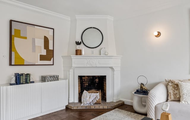 White fireplace with round mirror and abstract artwork.