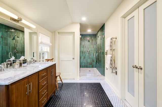 A modern bathroom with a double vanity, dark wood cabinets, a marble countertop, and a shower with green-tiled walls.