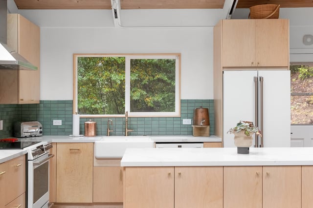 Modern light wood kitchen with teal tiles and white island.