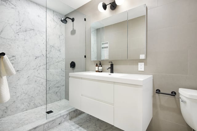A sleek, minimalist bathroom with marble-tiled walk-in shower, floating white vanity, and black accents.