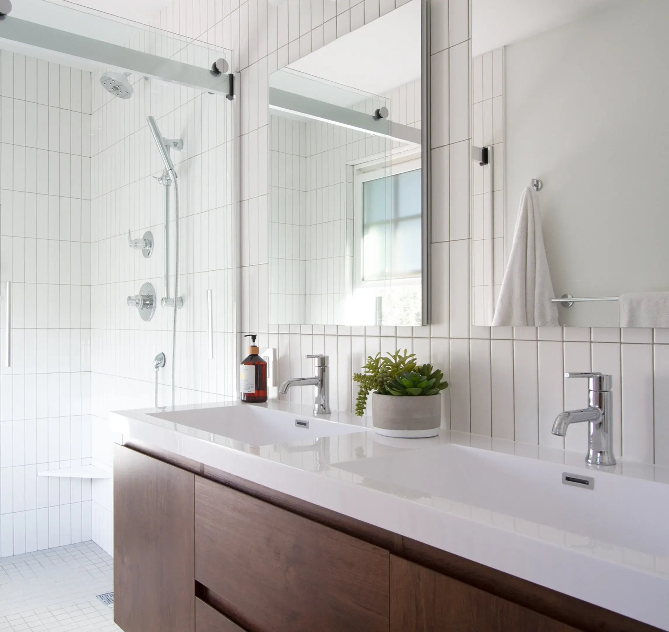 A modern, light-toned bathroom with glass shower and double-sink wood vanity.