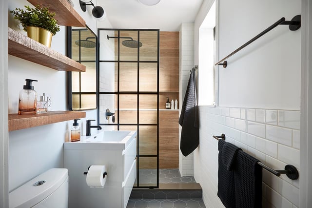 A modern bathroom with white subway tile, a white vanity, wood shelves, and a walk-in shower with a black-framed glass door and wood-look tile.