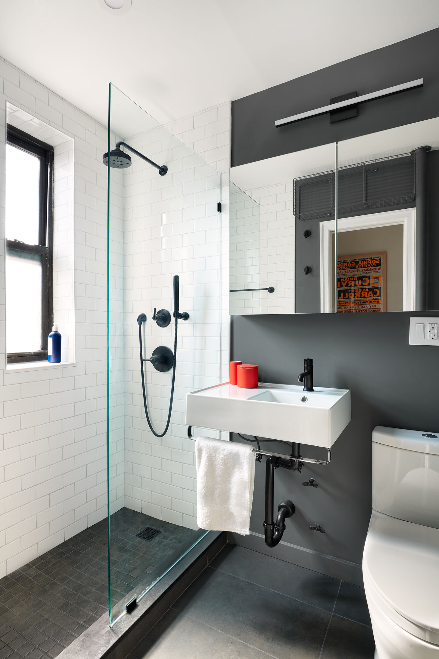 New York City bathroom with gray wall paint, white subway wall tiles, black tile flooring, a floating white vanity, walk-in shower, and matte black fixtures