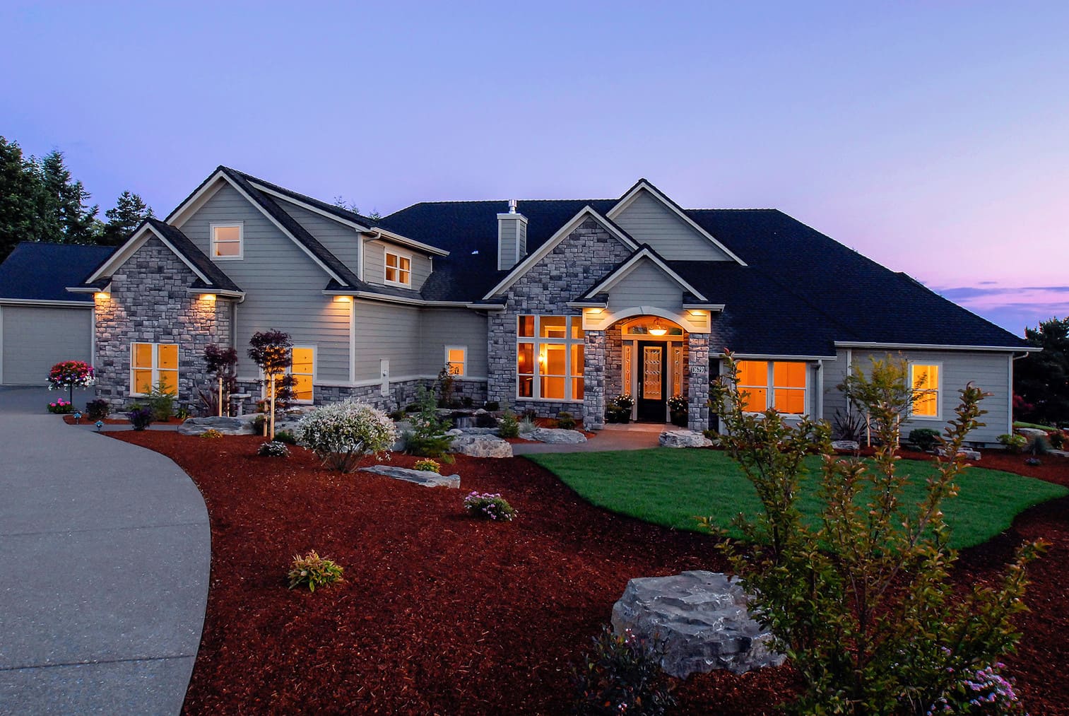 Modern suburban house at dusk with stone and wood siding.