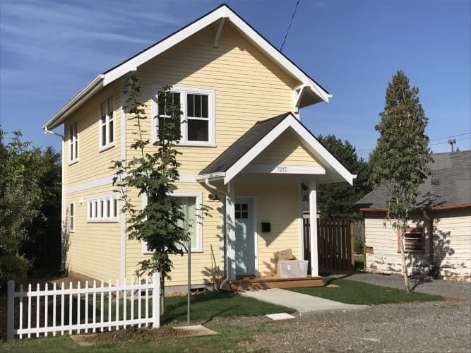  Yellow two-story ADU with white trim and picket fence.