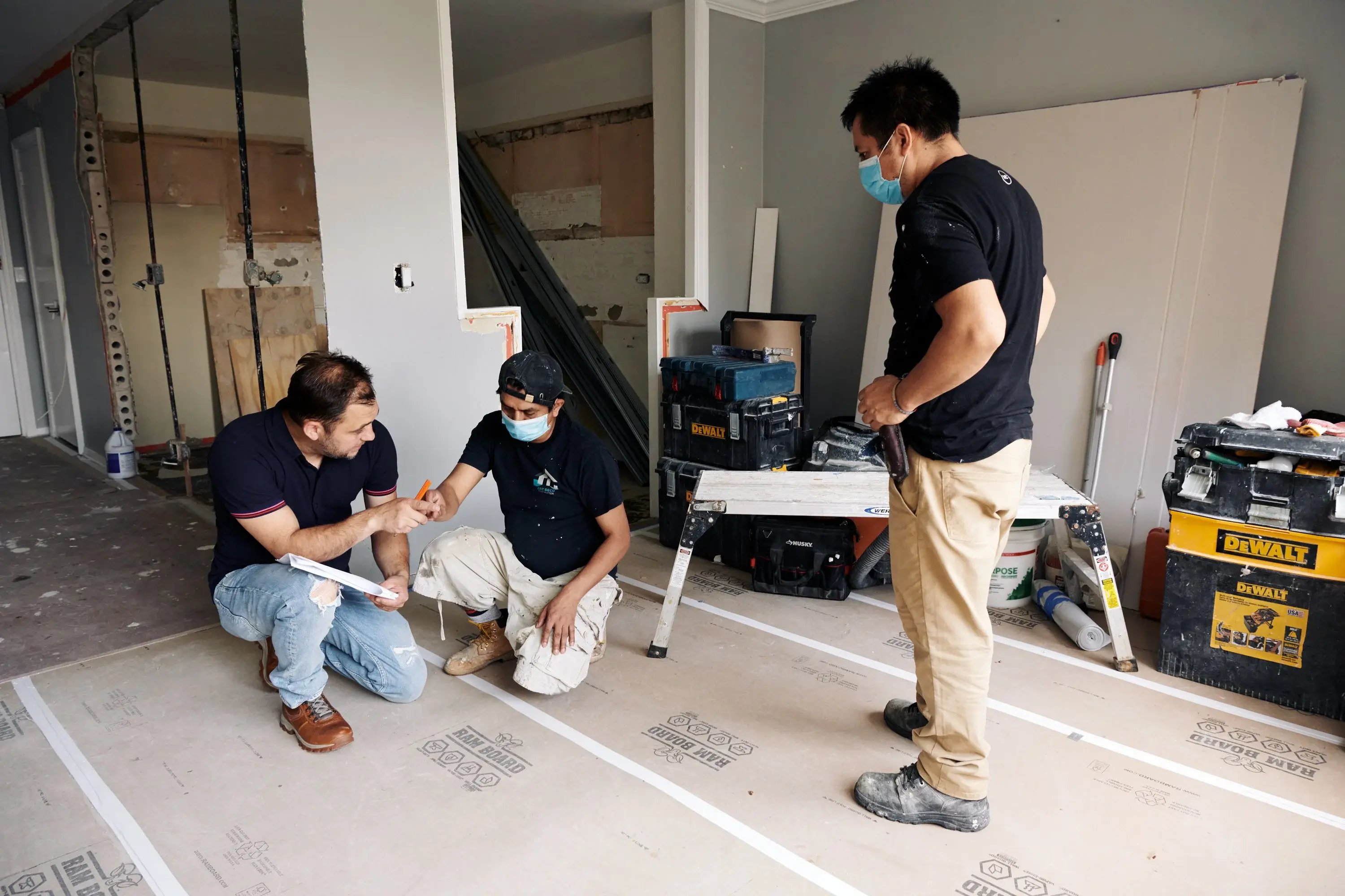 Three construction workers reviewing plans inside a partially renovated home.