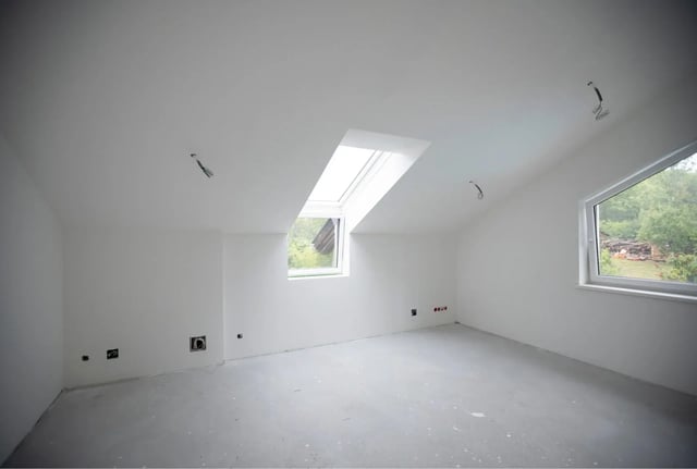  Empty white attic room with skylight and sloped ceiling.