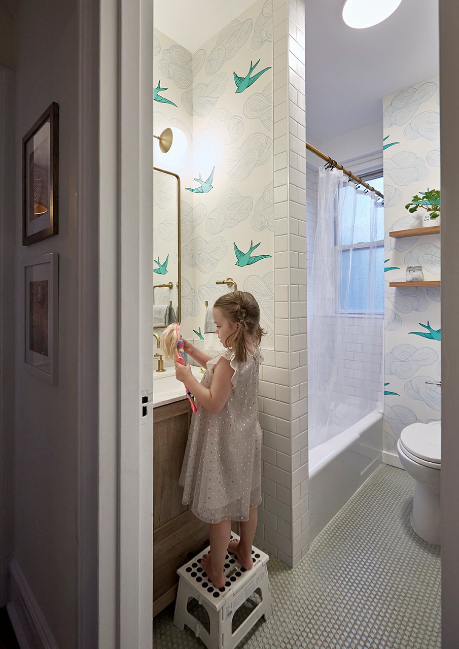 New York child's bathroom with penny floor tile, white subway tile, brass fixtures, and whimsical wallpaper with birds and clouds