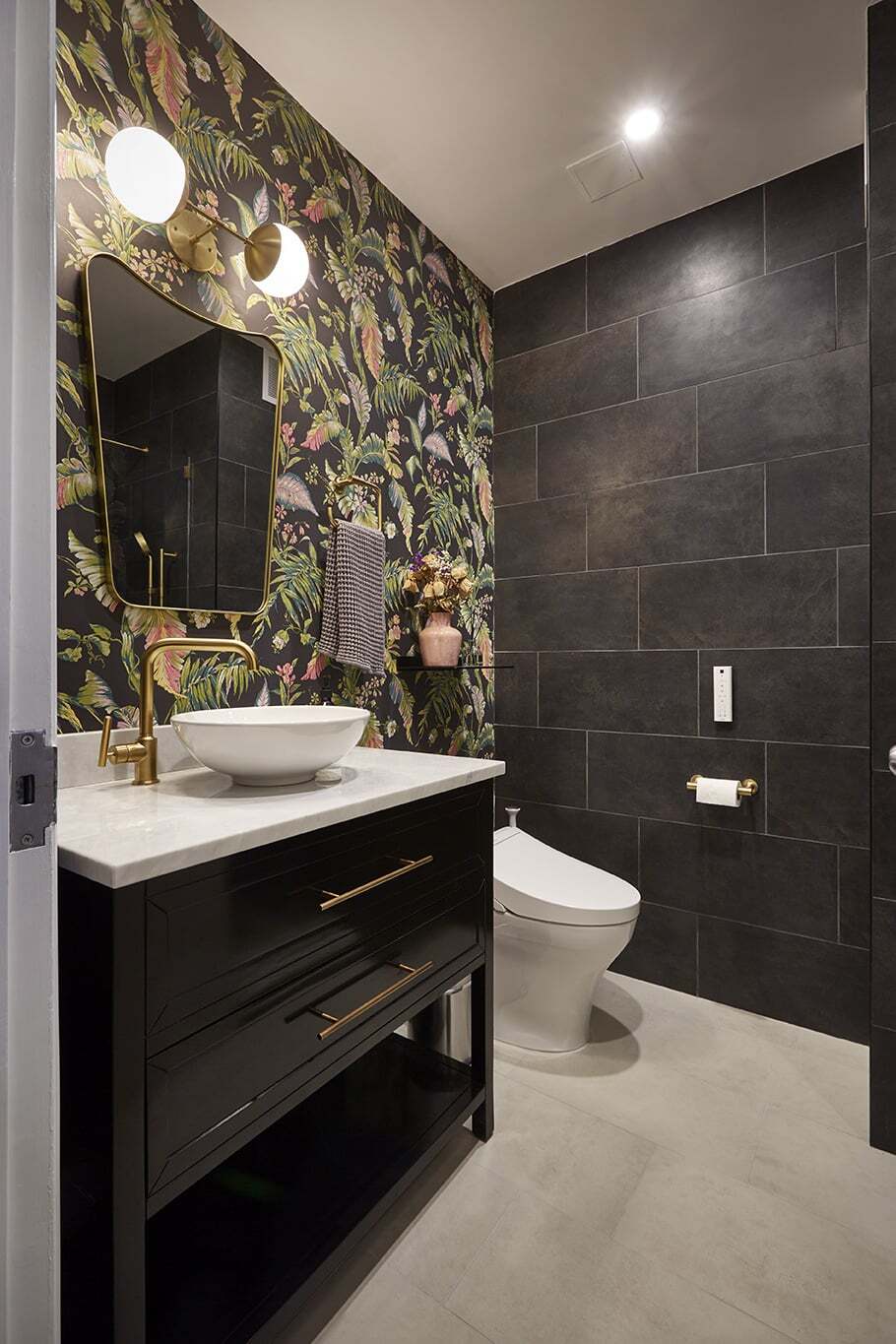 Modern dark bathroom with floral wallpaper and gold accents.