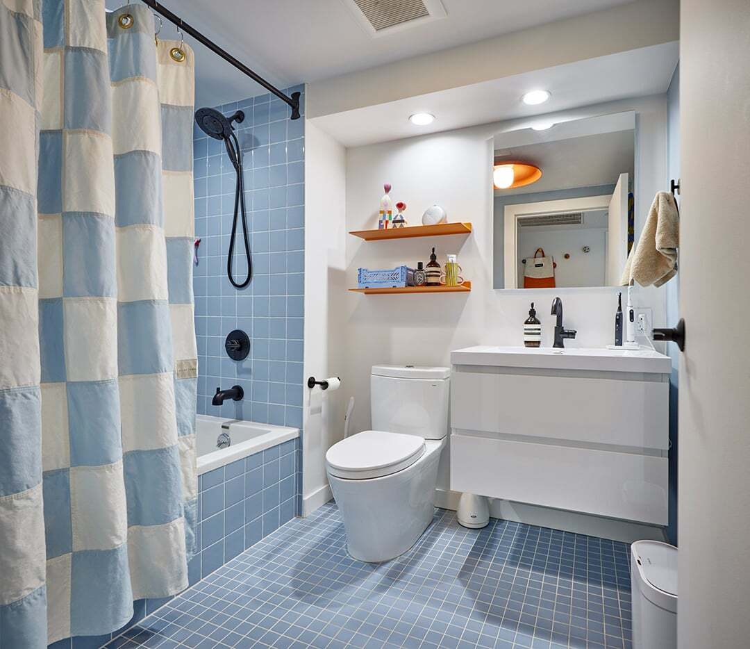 Light blue tiled bathroom with white vanity and orange shelf.