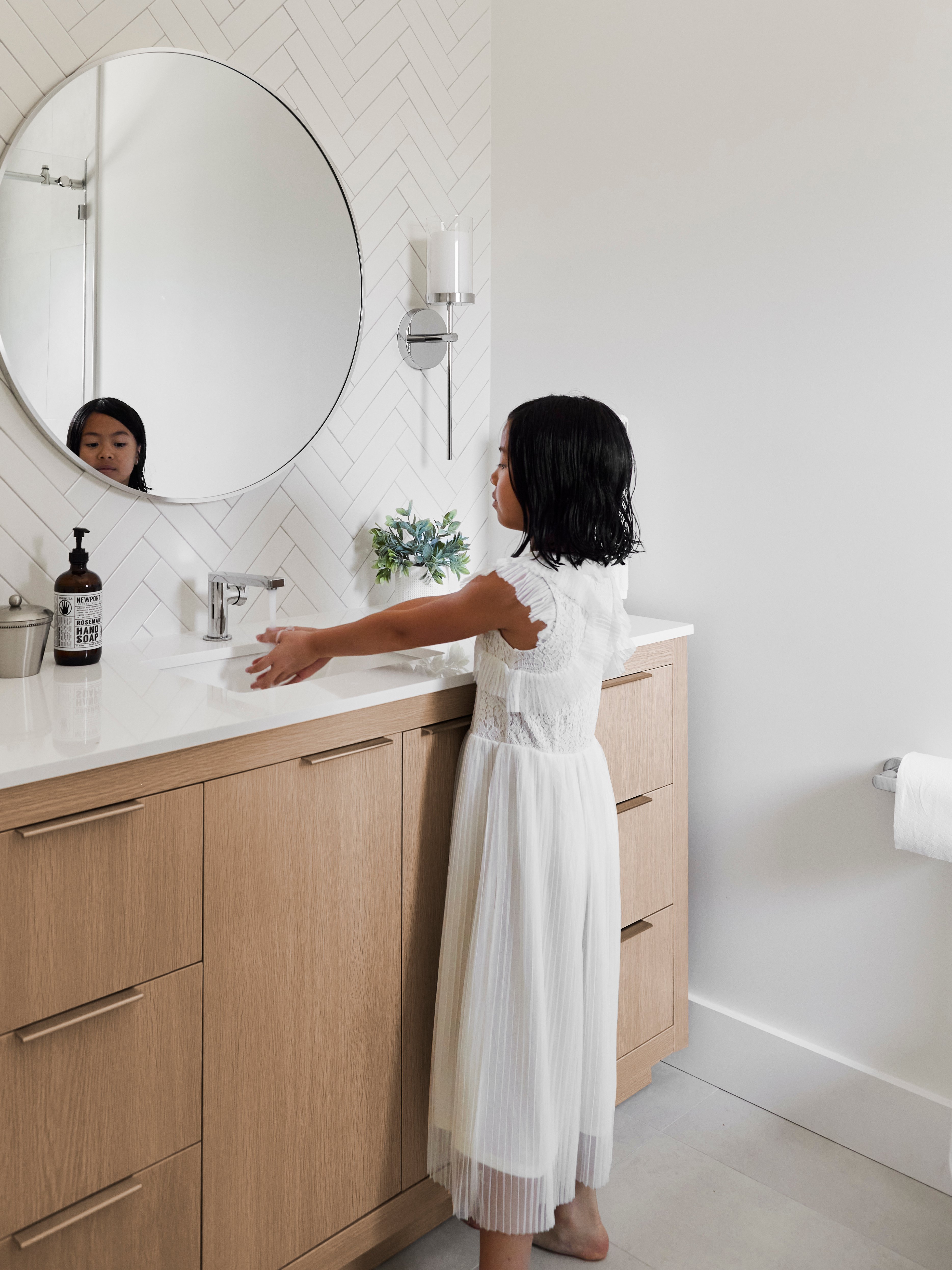 Child washing her hands in the sink of a Los Angeles bathroom with an extra large natural wood tone storage vanity