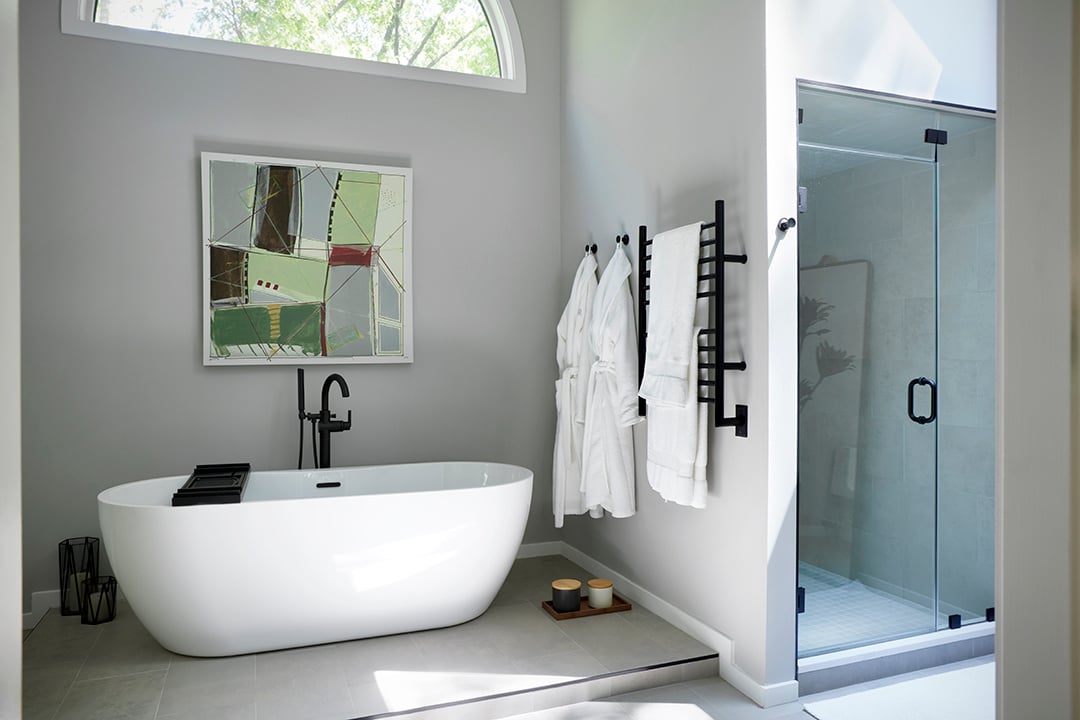 Remodeled bathroom in Westchester with a large soaking tub, walk-in shower with glass door, arched window, modern wall art, grey paint, gray floor tiles, and matte black fixtures.