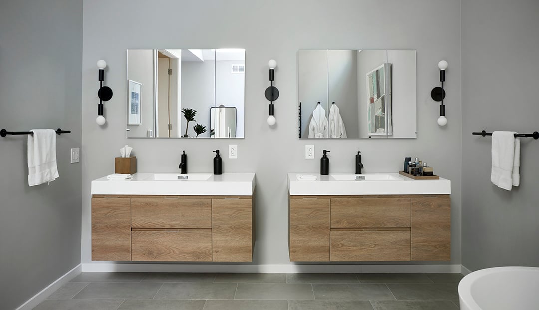 Primary bath with twin wooden vanities, matte black fixtures, gray painted walls, and gray flooring