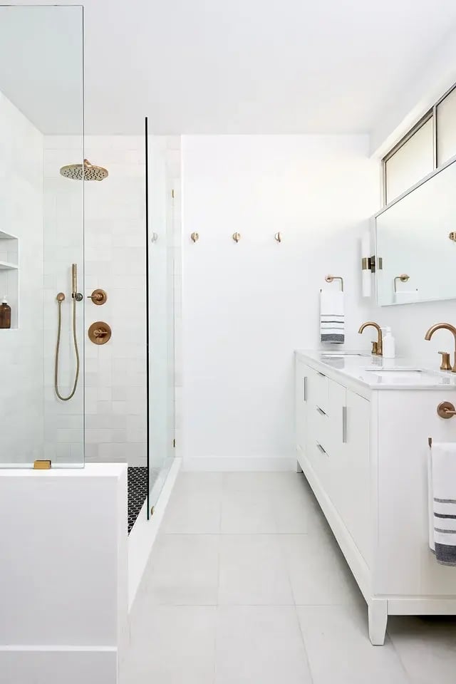  Bright white bath with brass fixtures and a double vanity.