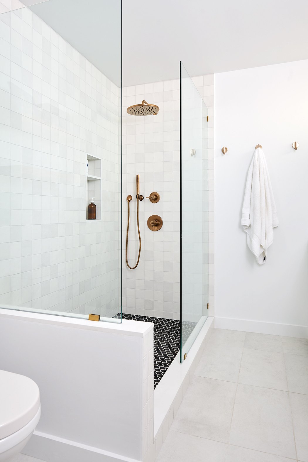 LA bathroom renovation with white walls and tiles, black hexagonal shower floor tile, brass fixtures, and a walk-in shower