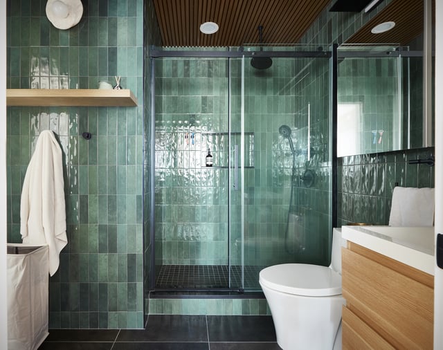 Bathroom with a curbed walk-in shower, with glass sliding doors, matte black fixtures, a wall niche, and glazed porcelain tile