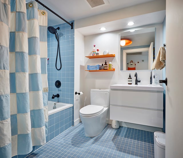 Kids' bathroom with complementary color scheme with blue floor and wall tiles, a blue checkerboard shower curtain, and orange accessories like floating shelves