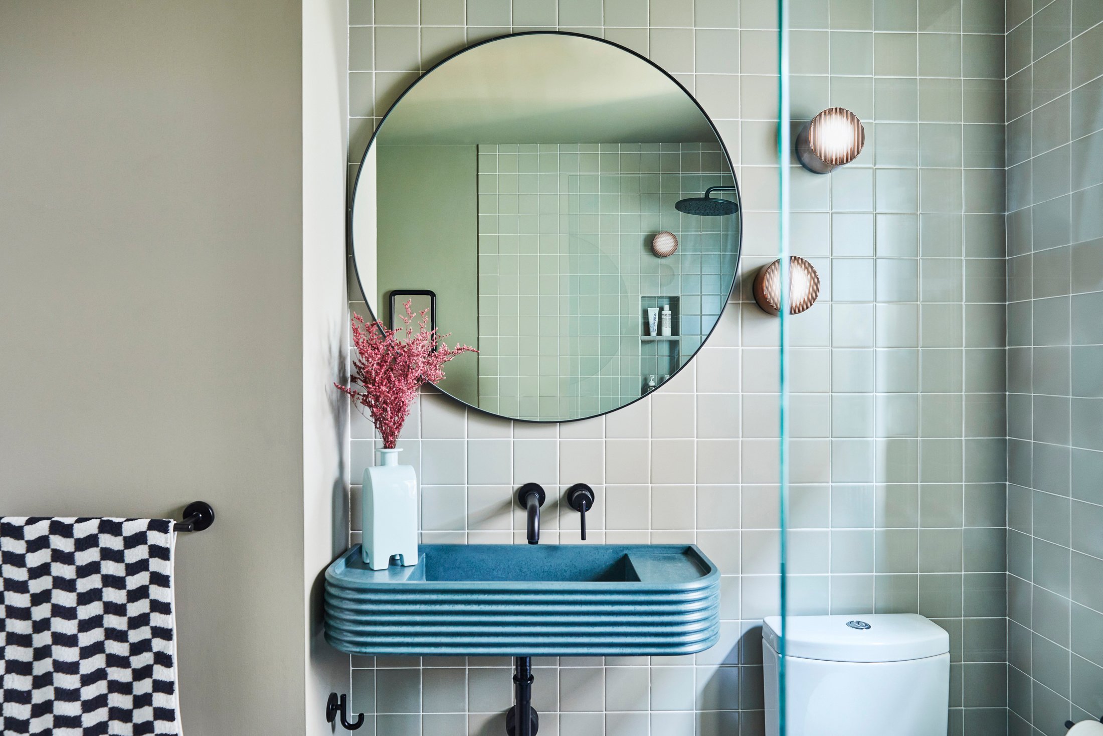 New Jersey bathroom renovation with green wall tile and paint, blue concrete floating sink, round mirror, and glass enclosure shower