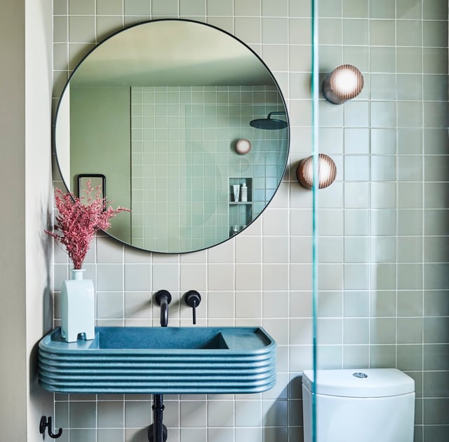 Contemporary bathroom with floating concrete vanity, round mirror, mint green square wall tile, and wall sconces