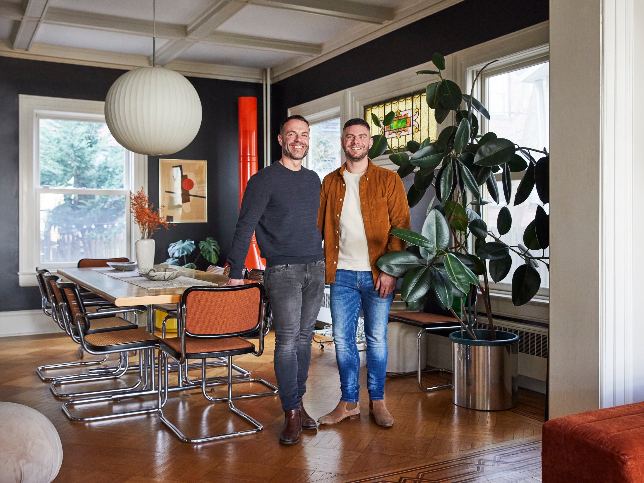 Homeowners in a restored brownstone with updated moldings, a stained glass window, modern furniture, and restored hardwood floors