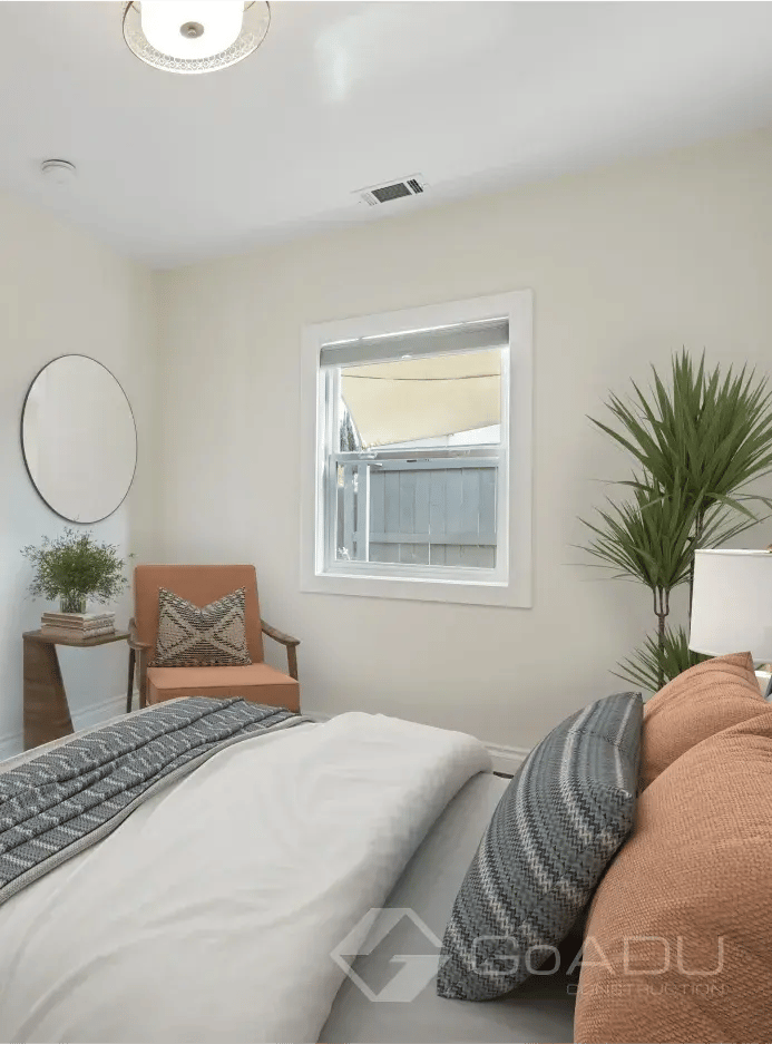 A bright and airy modern bedroom featuring neutral walls, a large green potted plant, and a stylish terracotta-colored accent chair tucked into a cozy corner by the window.