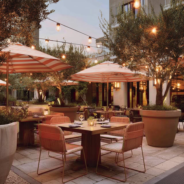 Chic patio with striped umbrellas, trees, and cozy lights.