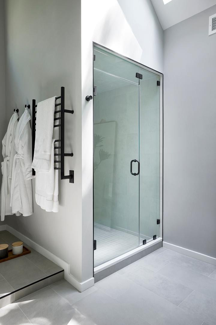 Modern glass shower with black hardware and white towels.