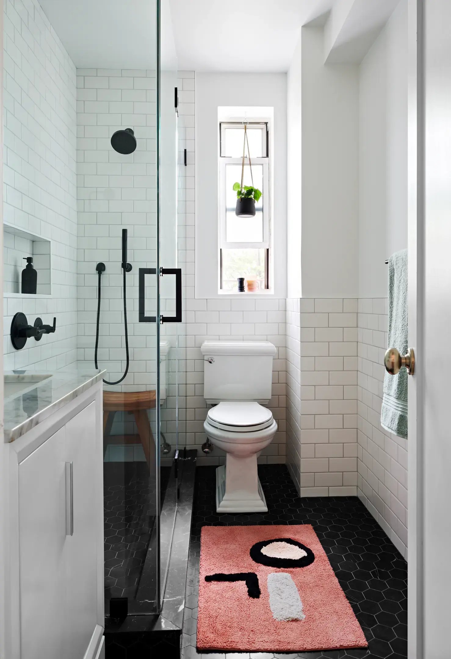 A compact bathroom featuring a black hexagonal tile floor contrasted by white subway wall tiles and sleek black hardware.