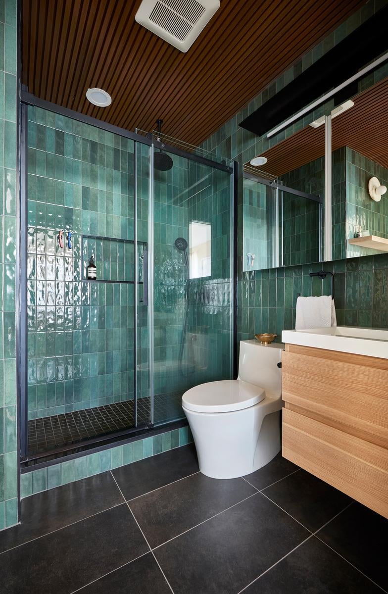 Green-tiled walk-in shower with glass enclosure, ceiling-mounted rain showerhead, built-in wall niche, wood slat ceiling, and modern fixtures for a spa-inspired bathroom upgrade.