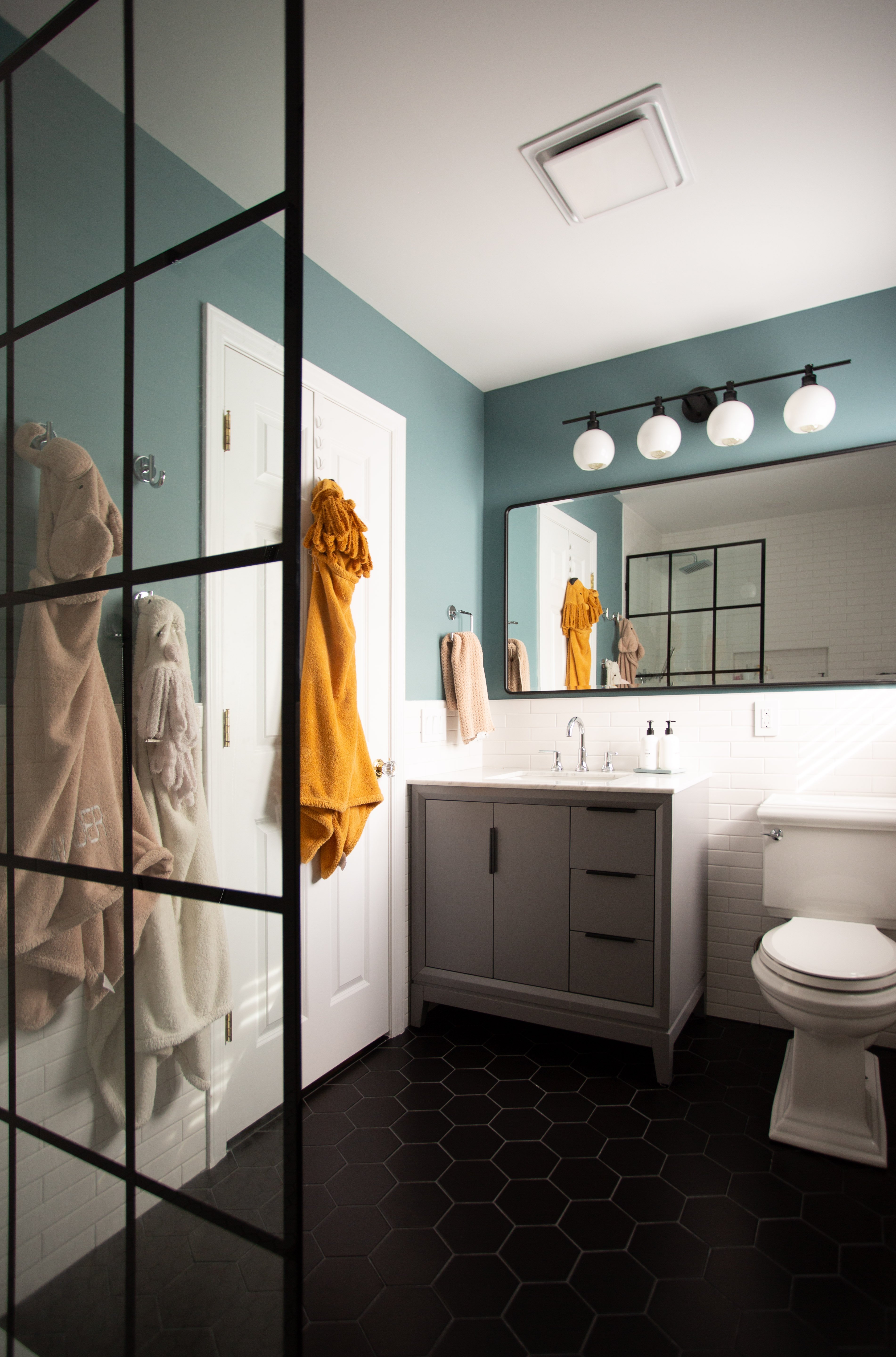 Children's bathroom with blue paint, white subway tile walls, black hexagonal flooring, and a large storage vanity