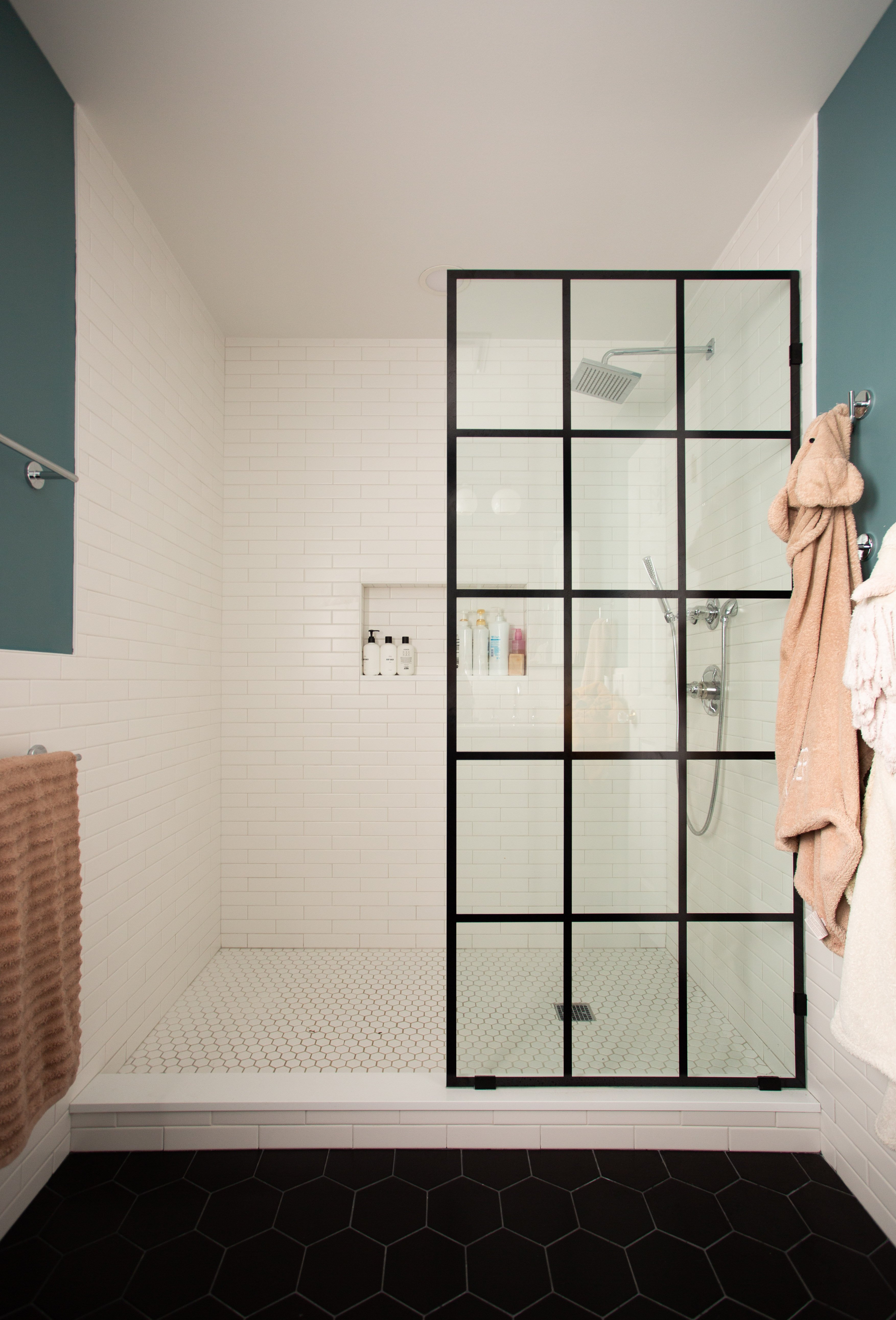 Tub to shower conversion for a children's bathroom, with matte black framed glass enclosure, polished chrome fixtures, black hexagonal floor tiles, and white subway wall tile