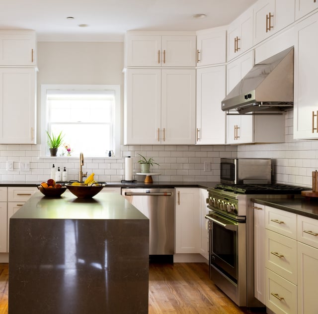 Remodeled kitchen with white cabinets, black countertops, hardwood floor, stainless steel appliances, and brass fixtures