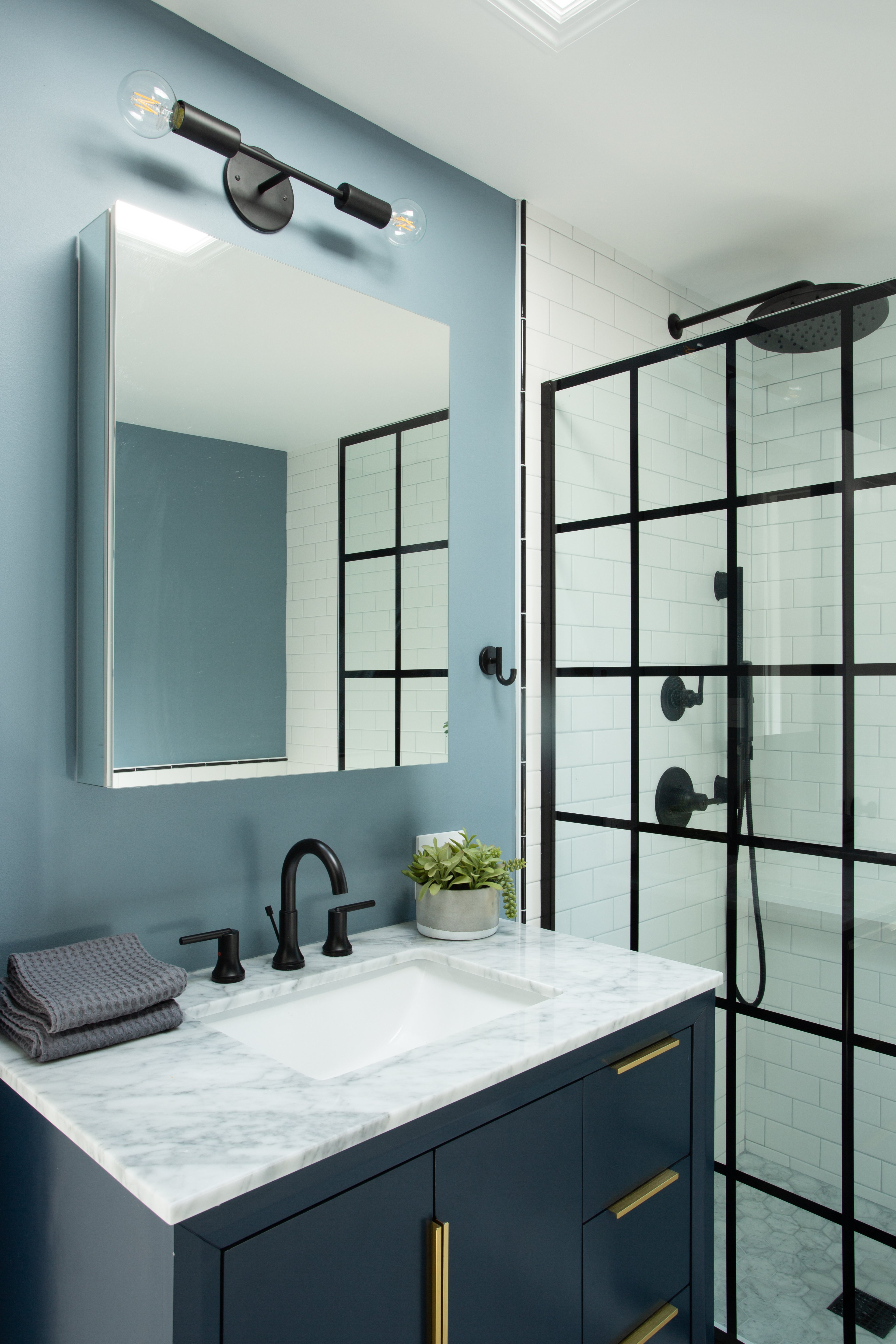 Bathroom with light blue walls, a navy vanity, white tiles, and black fixtures