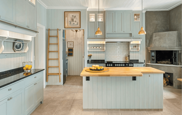 A light blue-green kitchen featuring a wooden ladder, a stove, a butcher block island, and a stone fireplace.