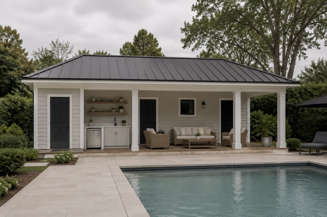 A pool house with a black metal roof, featuring a small outdoor kitchen and a covered seating area next to a swimming pool.