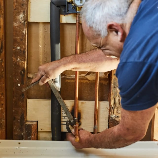 Plumber repairing copper pipes inside an exposed wall.