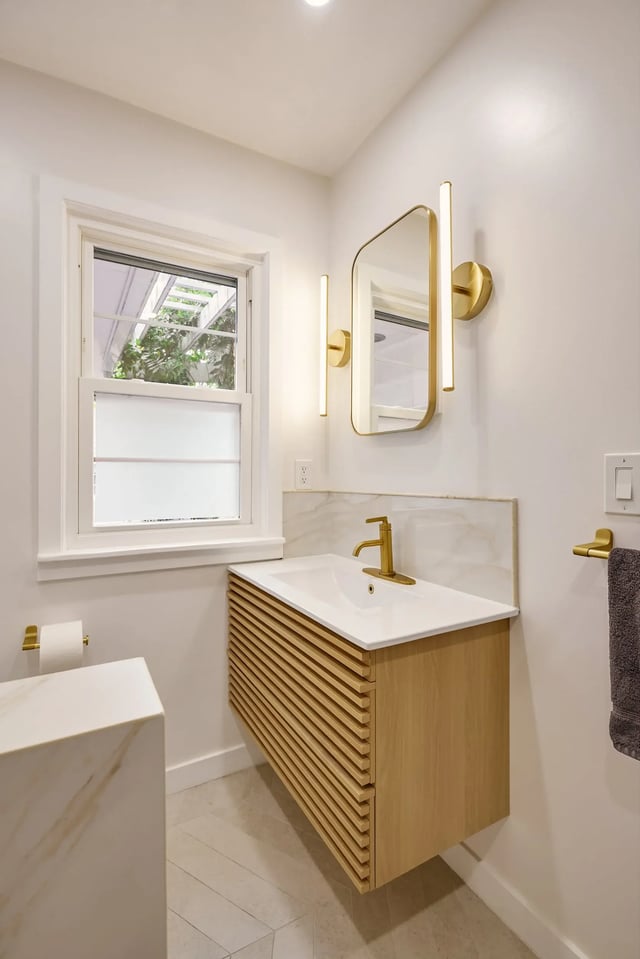 Beautiful modern bathroom features light wood vanity and gold accents.