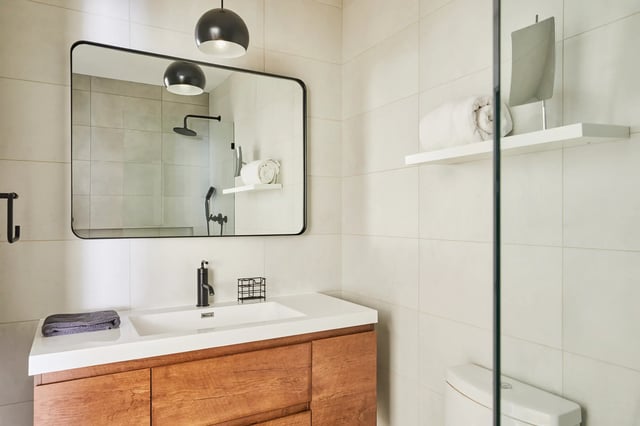 A modern bathroom with a wood vanity, a large mirror, and light-colored tile walls.