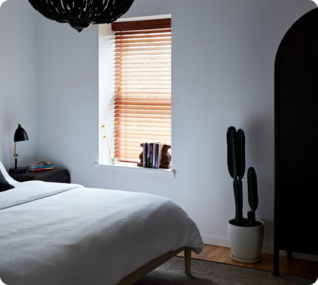 Bedroom with white bedding, wood blinds, a cactus, and armoire.