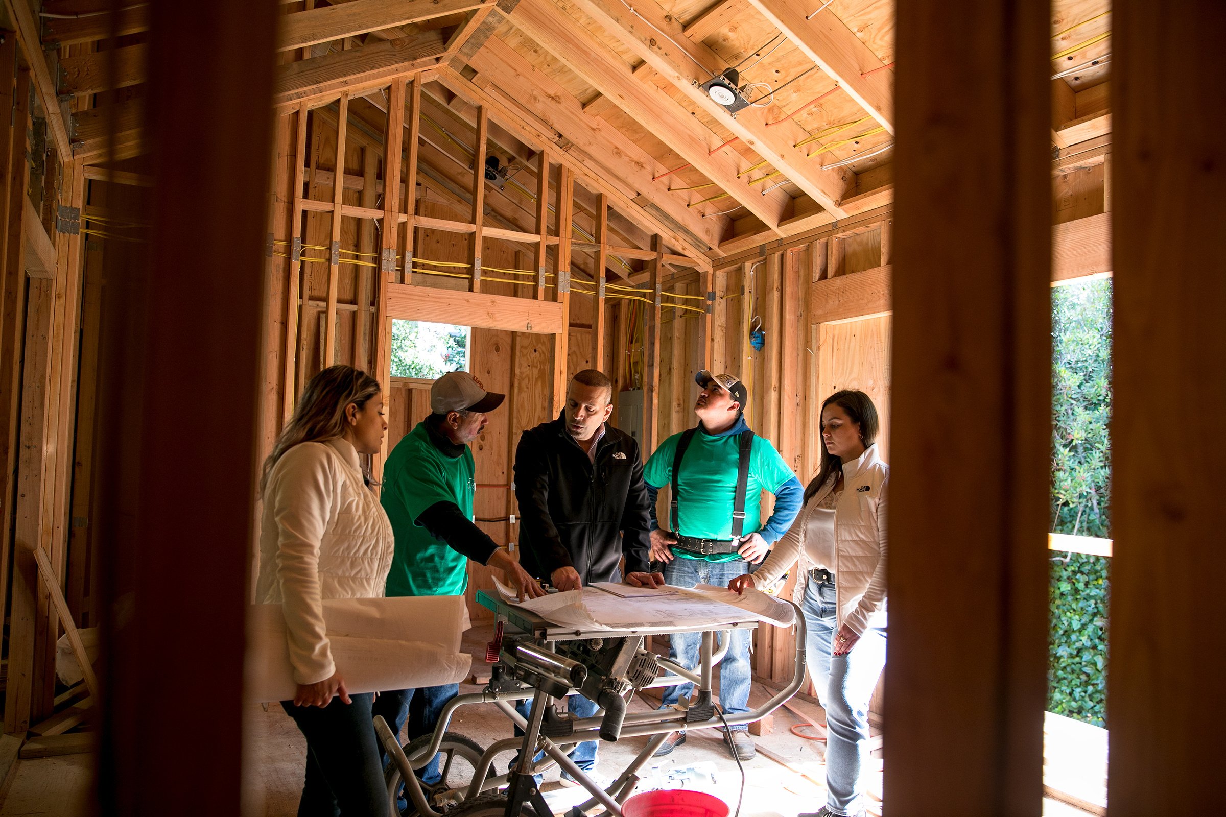 Construction team in a gut renovation looking over architectural plans and surrounded by studs and framing