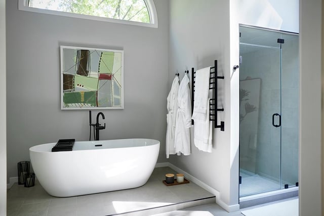 Modern grey bathroom with a freestanding white tub, glass shower, and art.