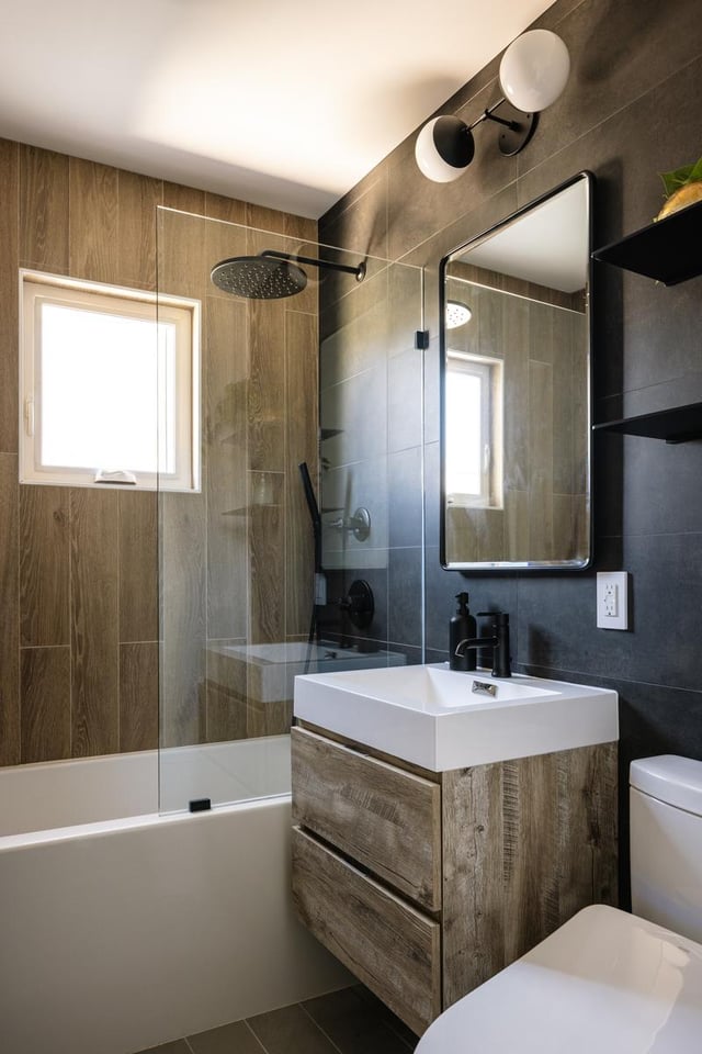 Modern bathroom with wood tile, glass splash, and rustic vanity.